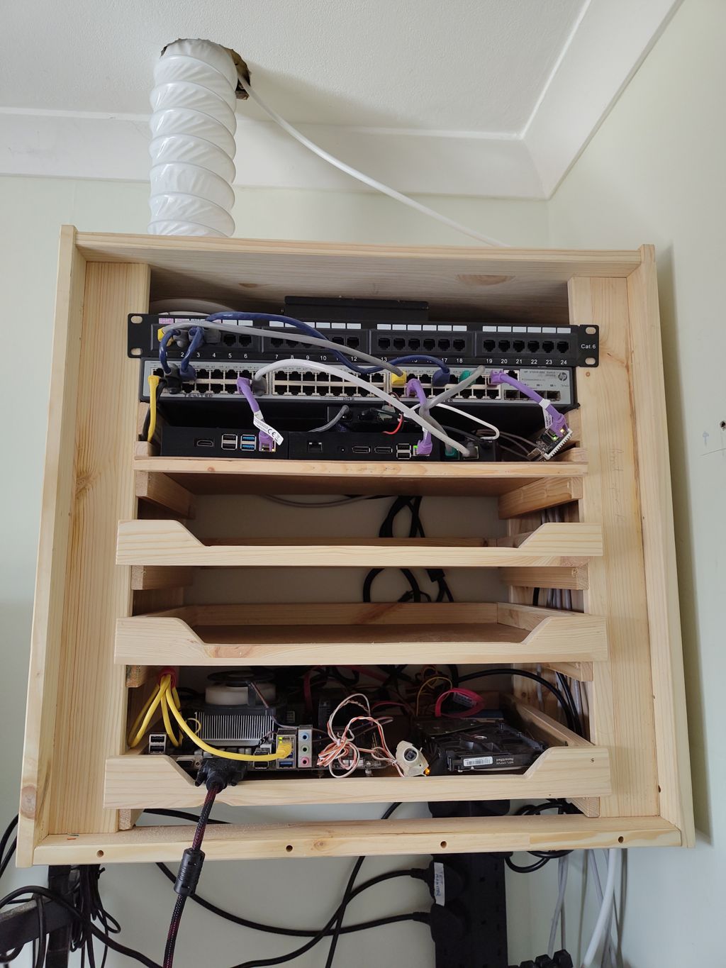Photo of a pine cabinet with a 1U switch, patch panel, four removable trays with various computers on them, and an extractor duct connected through the top panel.